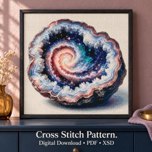 May include: A cross stitch pattern digital download featuring a geode design with a spiral galaxy center in shades of deep blue, purple, pink, and white. The artwork is framed in a dark square frame with the text Cross Stitch Pattern.
