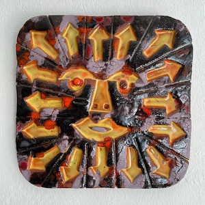 May include: A square ceramic wall art piece with a face design and yellow arrows. The face has orange eyes, a nose, and a mouth. The background is dark brown with red and purple accents. The piece is likely around 20 cm x 20 cm.
