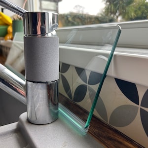 May include: Close-up of a chrome kitchen faucet with a gray rubberized handle. The faucet is mounted on a countertop with a glass splash guard.