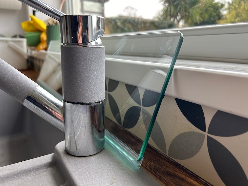 May include: Close-up of a chrome kitchen faucet with a gray rubberized handle. The faucet is mounted on a countertop with a glass splash guard.