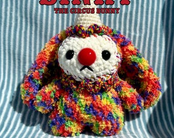 May include: A colorful crochet bunny toy with a clown-like appearance. The bunny has a white face, a red nose, and black eyes. The body is made of rainbow-colored yarn. Text on the image reads "BINKY THE CIRCUS BUNNY" and "CROCHET PATTERN".