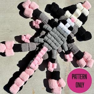 Könnte beinhalten: Ein großes, handgefertigtes Häkelprojekt in Form einer stilisierten Kreatur, mit rosa, schwarzem, grauem und weißem Garn. Das Design umfasst einen zentralen Körper und mehrere Anhänge. Der Text "PATTERN ONLY" befindet sich in einem rosa Kreis.