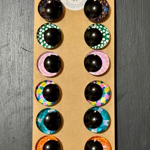 May include: A set of twelve glass cabochon eye designs in various colors and patterns, including starry night, green polka dots, pink crescent moon, and colorful abstract designs. The eyes are mounted on a brown card with the text "LIVVIES design".