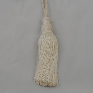 May include: A white tassel with a long, thin fringe. The tassel is made of a soft, natural fibre and has a simple, elegant design.