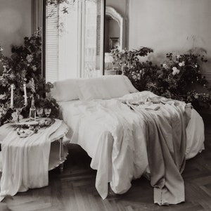 Puede incluir: Una cama blanca con s&aacute;banas blancas de lino y una manta blanca. La cama est&aacute; en una habitaci&oacute;n con una ventana y plantas.
