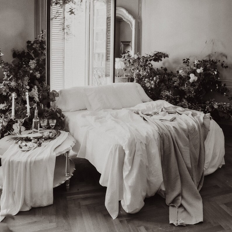 Puede incluir: Una cama blanca con s&aacute;banas blancas de lino y una manta blanca. La cama est&aacute; en una habitaci&oacute;n con una ventana y plantas.