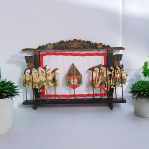 Pode incluir: Um palco de fantoches de sombras de madeira com um pano de fundo branco e uma coleção de fantoches de sombras coloridos pintados à mão. Os fantoches estão em paus e estão prontos para serem usados para uma apresentação.