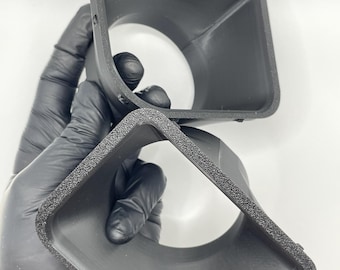 Może przedstawiać: Dwa czarne plastikowe osłony obiektywu aparatu z teksturą gumową krawędzią. Osłony są ułożone jedna na drugiej.