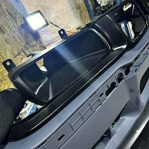 May include: A black plastic car bumper with a large black plastic grille. The bumper is painted a light gray color.