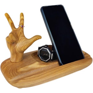Könnte beinhalten: Holzhandförmiger Organizer mit einem Telefonständer, einem Uhrenhalter und einem Ringhalter. Die Hand ist aus Holz geschnitzt und hat eine natürliche Oberfläche. Der Telefonständer ist aus Holz und hat eine schwarze Oberfläche. Der Uhrenhalter ist aus Holz und hat eine schwarze Oberfläche. Der Ringhalter ist aus Holz und hat eine natürliche Oberfläche.