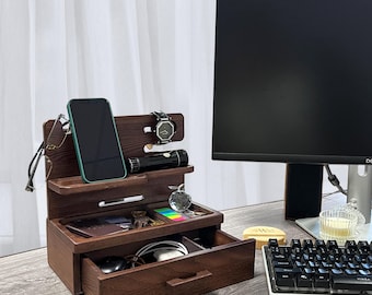May include: A dark brown wooden desk organizer with a drawer, a shelf for a phone, a watch holder, and a small compartment for other items. The organizer is on a desk with a keyboard and a computer monitor.