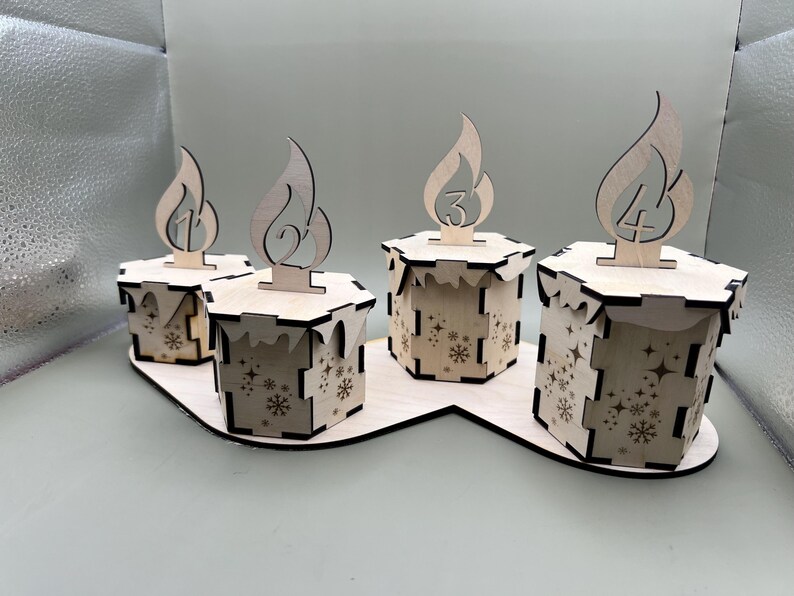 May include: Four wooden candle holders with numbers 1 through 4 on them. The holders are arranged in a row on a wooden base. Each holder has a snowflake design.