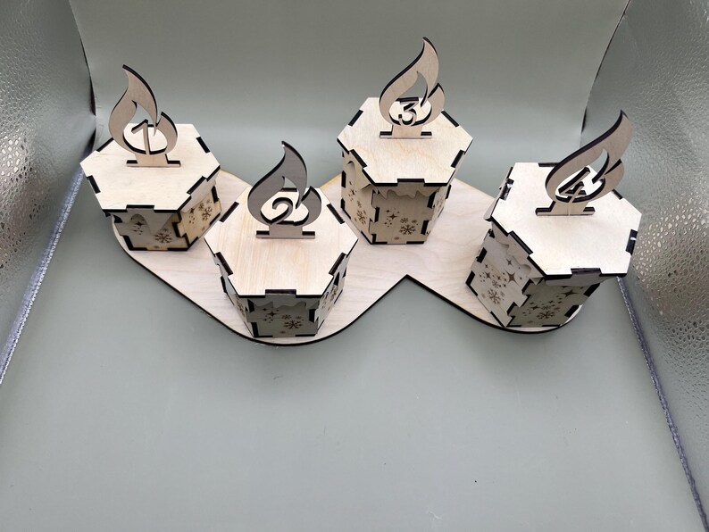 May include: Four wooden advent calendar boxes with a flame design and numbers 1 through 4. The boxes are arranged in a curved line on a wooden base.