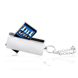 Può includere: Una chiavetta USB in metallo color argento con corpo rettangolare e porta di connessione interna blu. Il dispositivo presenta un piccolo anello metallico fissato a un'estremità, collegato a una corta e sottile catenella argentata come portachiavi.