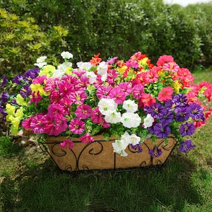May include: A black metal planter filled with a variety of colorful artificial flowers. The flowers are in shades of pink, purple, white, yellow, and red. The planter is sitting on a bed of green grass.