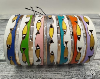 Op de afbeelding: Een set van acht leren armbanden met een witte achtergrond en een herhalend patroon van gele vissen met zwarte ogen. De armbanden zijn in verschillende kleuren, waaronder blauw, groen, roze, grijs, turquoise, oranje en paars.