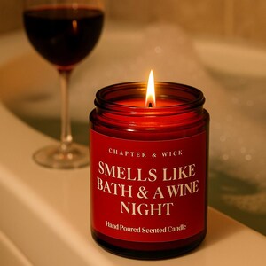 May include: A lit red candle in a glass jar with the text "Smells Like Bath & A Wine Night" on a red label. A wine glass with red wine is in the background. The candle is hand-poured and scented.