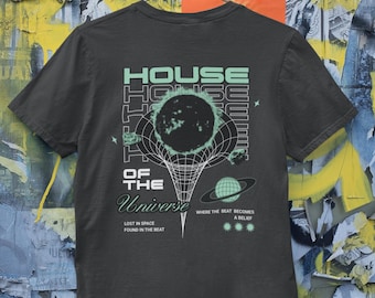 May include: Dark gray t-shirt with a graphic design featuring the text "HOUSE OF THE UNIVERSE" in a retro font, along with a celestial illustration. The shirt also includes the phrases "LOST IN SPACE FOUND IN THE BEAT" and "WHERE THE BEAT BECOMES A BELIEF."