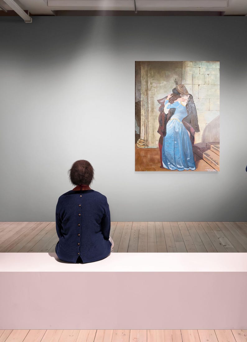Puede incluir: Interior de una galer&iacute;a de arte con una persona sentada en un banco blanco, mirando una pintura. La pintura muestra a una mujer con un vestido azul y un hombre abraz&aacute;ndose. Las paredes son grises y el suelo es de madera.