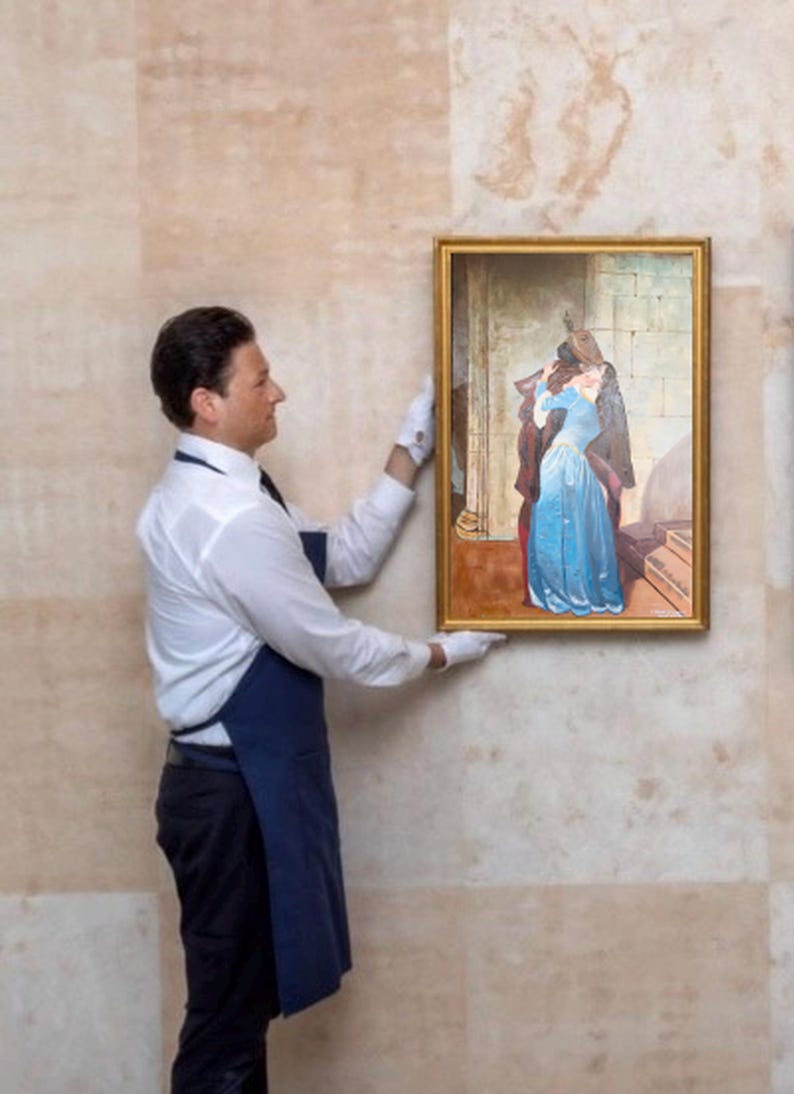 Puede incluir: Un cuadro enmarcado que representa a una pareja abraz&aacute;ndose, la mujer con un vestido azul. El cuadro lo sostiene una persona con camisa blanca, pantal&oacute;n negro, delantal azul y guantes blancos. El marco es dorado.