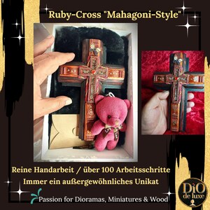 K&ouml;nnte beinhalten: Handgefertigtes Holzkreuz im Mahagoni-Stil mit aufwendigen Details und einem roten Edelstein in der Mitte. Ein kleiner rosa Teddyb&auml;r ist enthalten. Der Text lautet "Ruby-Cross Mahagoni-Style".