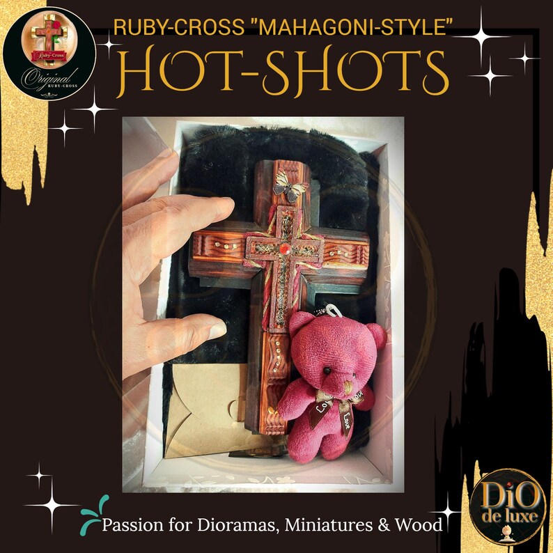 K&ouml;nnte beinhalten: Ein Holzkreuz im Mahagoni-Stil mit aufwendigen Schnitzereien und einem roten Edelstein. Ein kleiner rosa Teddyb&auml;r mit Schleife ist enthalten. Der Text "RUBY-CROSS MAHAGONI-STYLE HOT-SHOTS" ist sichtbar.