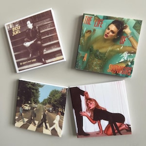 Könnte beinhalten: Vier quadratische Magnete mit Albumcovern. Einer zeigt Billy Joel, ein anderer eine Frau im Wasser, ein dritter zeigt die Beatles, die den Abbey Road überqueren, und der letzte zeigt eine Frau auf Knien.