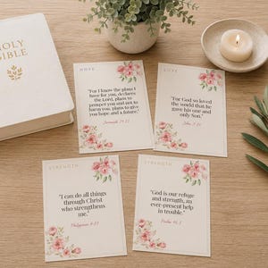 Op de afbeelding: Een witte Bijbel, vier rechthoekige kaarten met bloemaccenten en Bijbelverzen, een kleine potplant en een witte kaars in een schaaltje. De kaarten bevatten de woorden Hope, Love en Strength naast teksten uit Jeremia, Johannes en de Psalmen.