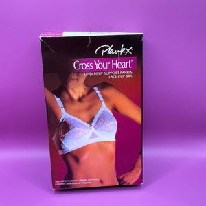 May include: A Playtex "Cross Your Heart" bra box. The box features a white lace bra with undercup support panels. The text on the box reads "Special criss-cross design provides comfort and natural shaping."
