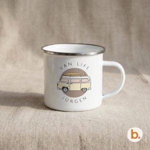 A white enamel mug features a yellow campervan illustration inside a brown circle and the custom name JÜRGEN.