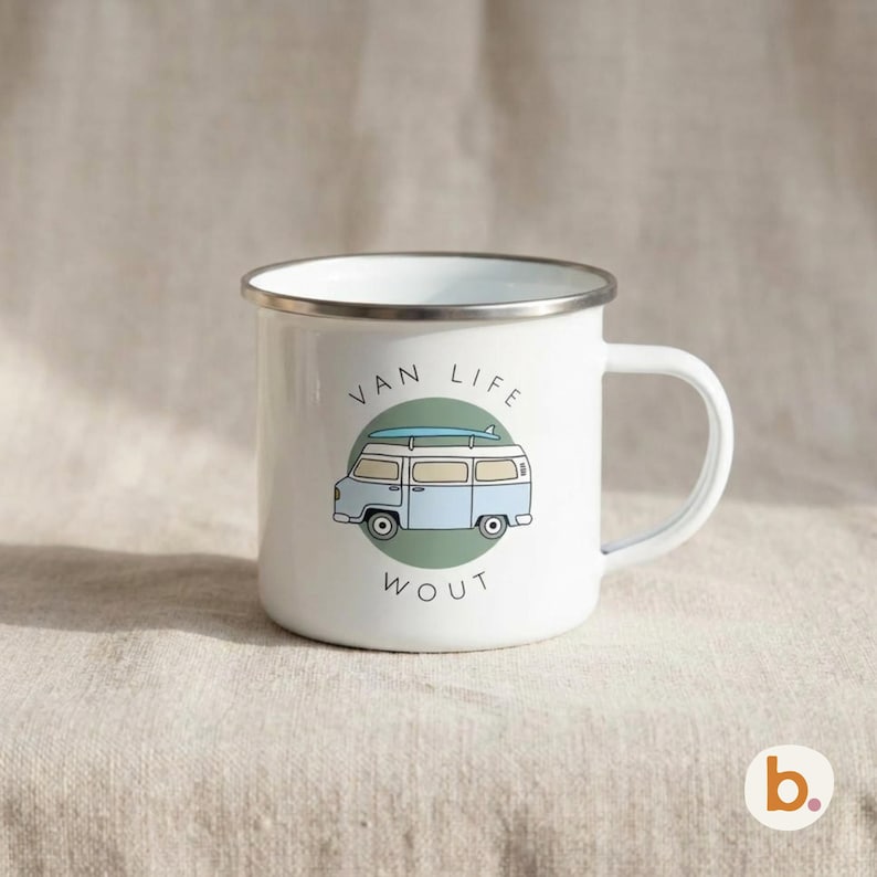 A white enamel mug with a silver rim rests on a textured surface, showing a blue campervan graphic and the text VAN LIFE WOUT.