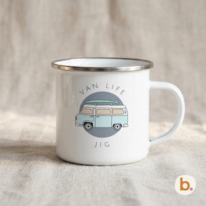 A white enamel camping mug features an illustration of a light blue campervan over a gray circle and the custom text JIG.
