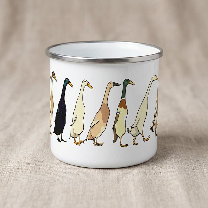 A white enamel camping mug printed with a line of cartoon runner ducks in various colors, displayed on a burlap surface.