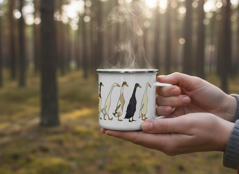 Hands holding a steaming enamel mug with a runner duck graphic against a softly lit pine forest background.