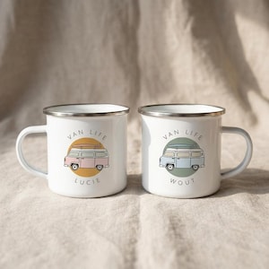 Two white enamel campervan mugs with personalized names Lucie and Wout displayed on a neutral fabric background.
