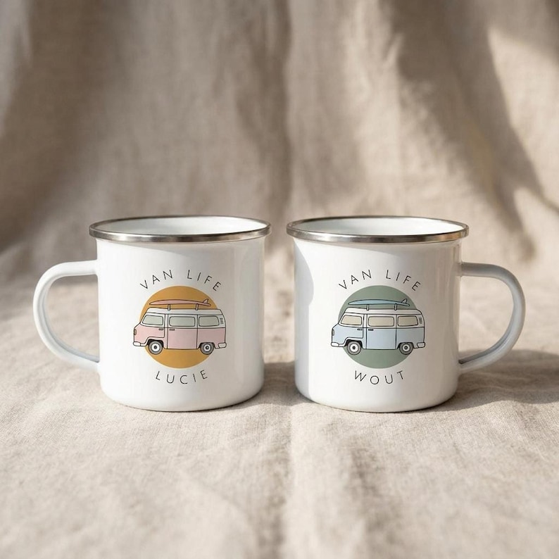 Two white enamel campervan mugs with personalized names Lucie and Wout displayed on a neutral fabric background.