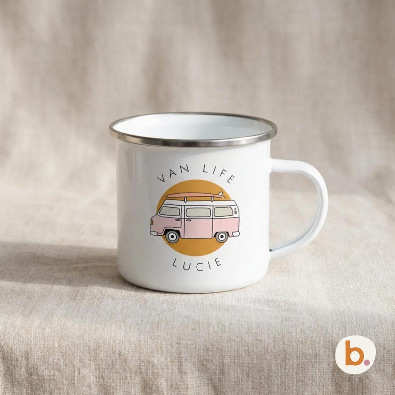 A white enamel mug with a silver rim sits on a neutral fabric background, featuring a pink campervan illustration and the text VAN LIFE LUCIE.