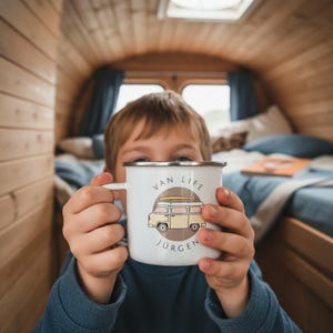 A young boy holds a white enamel mug with a yellow campervan illustration and the name Jurgen inside a wooden camper interior.