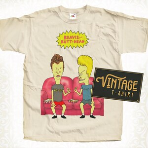 May include: Cream-coloured t-shirt featuring a cartoon image of Beavis and Butt-Head sitting on a red couch. The shirt has the text "BEAVIS and BUTT-HEAD" in a yellow burst and a black sign that says "VINTAGE T-SHIRT".