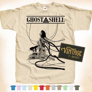 Könnte beinhalten: Beiges T-Shirt mit einer Schwarz-Weiß-Grafik von "Ghost in the Shell". Das Design enthält den Text "Ghost in the Shell" über einer Illustration einer knienden Figur, die mit Drähten verbunden ist. Ein "Vintage T-Shirt"-Etikett ist ebenfalls vorhanden.