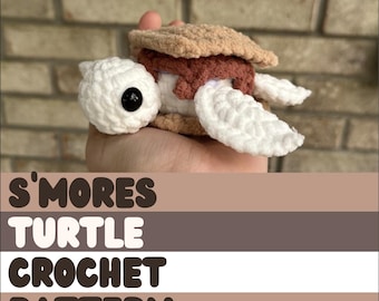 Puede incluir: Un juguete de amigurumi de tortuga tejido a crochet con forma de s'more. La tortuga es blanca con detalles marrones y rosados. El juguete está siendo sostenido en una mano. El texto "S'mores Turtle Crochet Pattern" está debajo de la imagen.