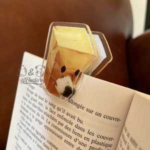 Peut inclure: Un marque-page en acrylique transparent représentant un chien de dessin animé portant un sac en papier brun sur la tête. Le marque-page est conçu pour maintenir une page dans un livre.