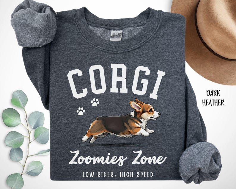 May include: Dark heather gray sweatshirt with the word "CORGI" in white block letters above a graphic of a running corgi dog. The text "Zoomies Zone" and "LOW RIDER, HIGH SPEED" are below the dog illustration. The sweatshirt has a crew neck and long sleeves.