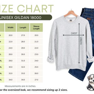 May include: A light gray Gildan 18000 unisex sweatshirt with a size chart. The chart shows measurements in inches for width, length, and sleeve length. Blue jeans are next to the sweatshirt. A small dog illustration is in the bottom right corner.