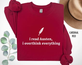 May include: A cardinal red sweatshirt with the text "i read Austen, i overthink everything" in white. A white feather graphic is above the text. The words "Cardinal Red" are written in black on the right side of the image.
