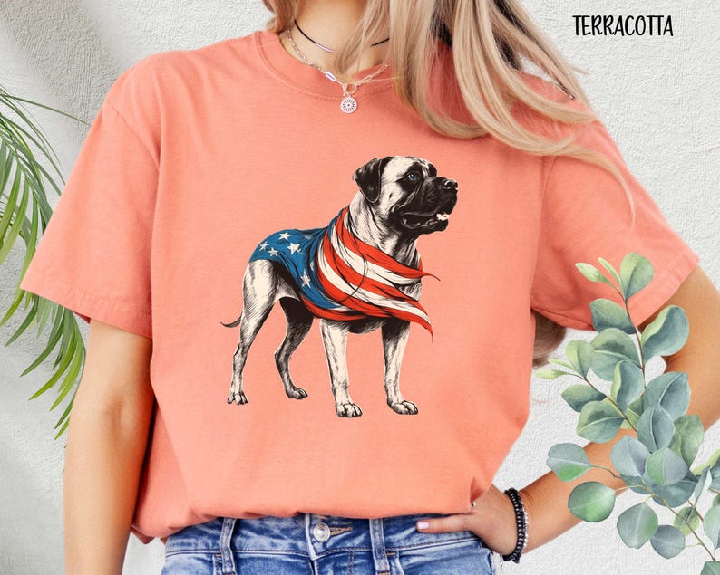 May include: A terracotta colored t-shirt with a graphic of a dog wearing an American flag. The dog is a Bullmastiff breed.