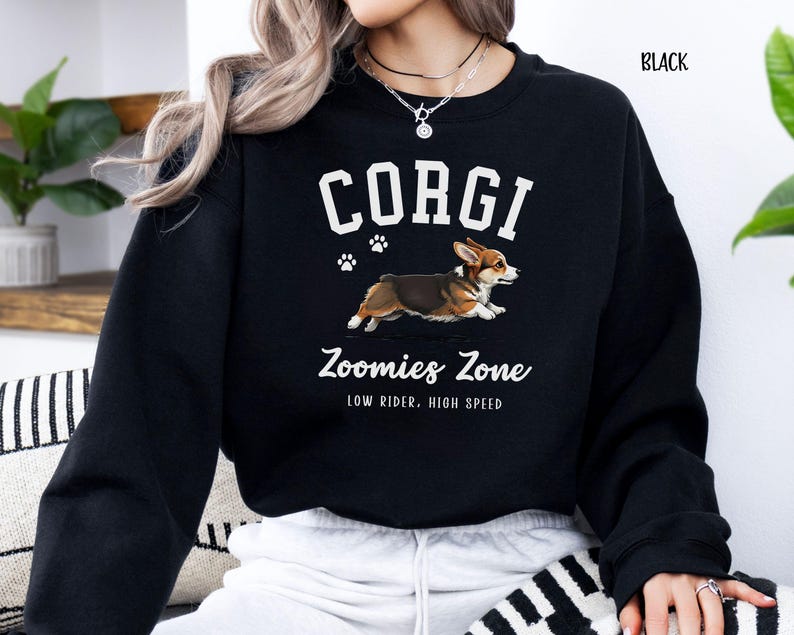 May include: Black sweatshirt featuring a graphic of a running corgi dog with the word "CORGI" above it. Below the dog is the text "Zoomies Zone" and "LOW RIDER, HIGH SPEED". The word "BLACK" is in the upper right corner.