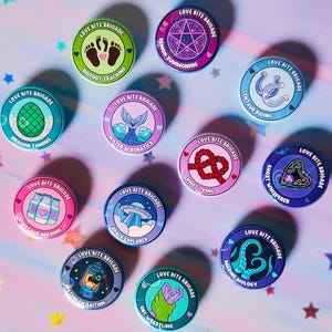 Könnte beinhalten: Eine Sammlung runder Anstecknadeln mit dem Text "LOVE BITE BRIGADE" und verschiedenen Illustrationen. Designs umfassen einen Bigfoot-Fußabdruck, ein Pentagramm, ein Hufeisen, ein Drachenei, einen Meerjungfrauenschwanz, einen Knoten, einen Geist, ein UFO, eine Laterne und einen Oktopus. Der Text "NONHUMAN ROMANCE MERIT BADGES" ist ebenfalls vorhanden.