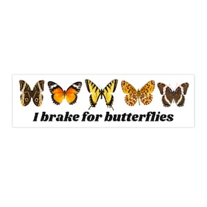 Puede incluir: Una pegatina de parachoques blanca con cinco mariposas diferentes en fila. Las mariposas son marrones, naranjas, amarillas, marrones y blancas. El texto "I brake for butterflies" está debajo de las mariposas.