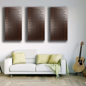 May include: Three rectangular, dark brown wall panels with horizontal black lines. The panels are mounted above a white sofa with yellow pillows. A guitar and floor lamp are also in the room.